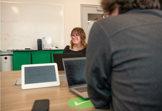 In this image, a woman discusses something with the team and laughs.